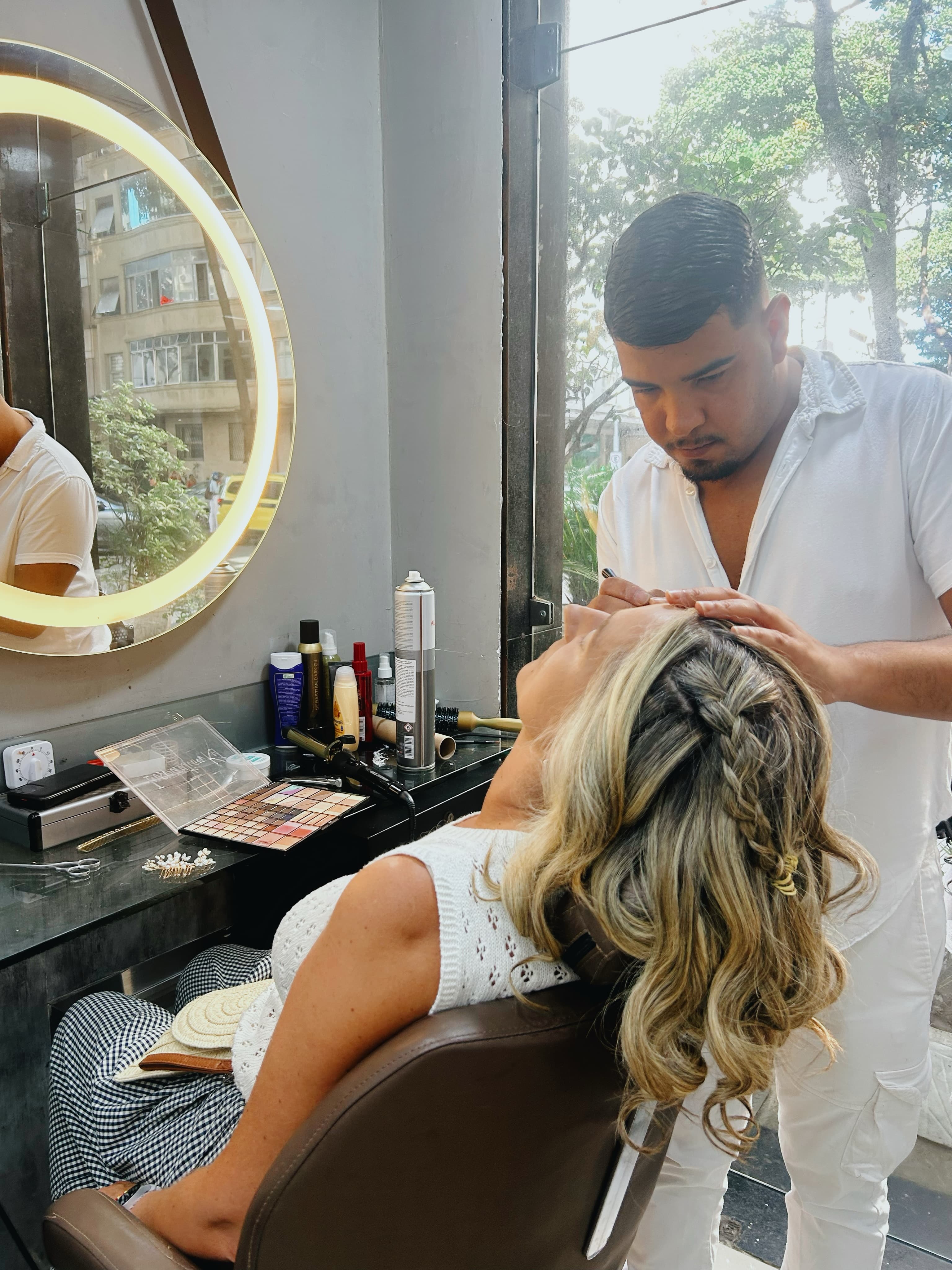 Cliente com maquiagem e penteado feitos no salão, em frente ao espelho iluminado